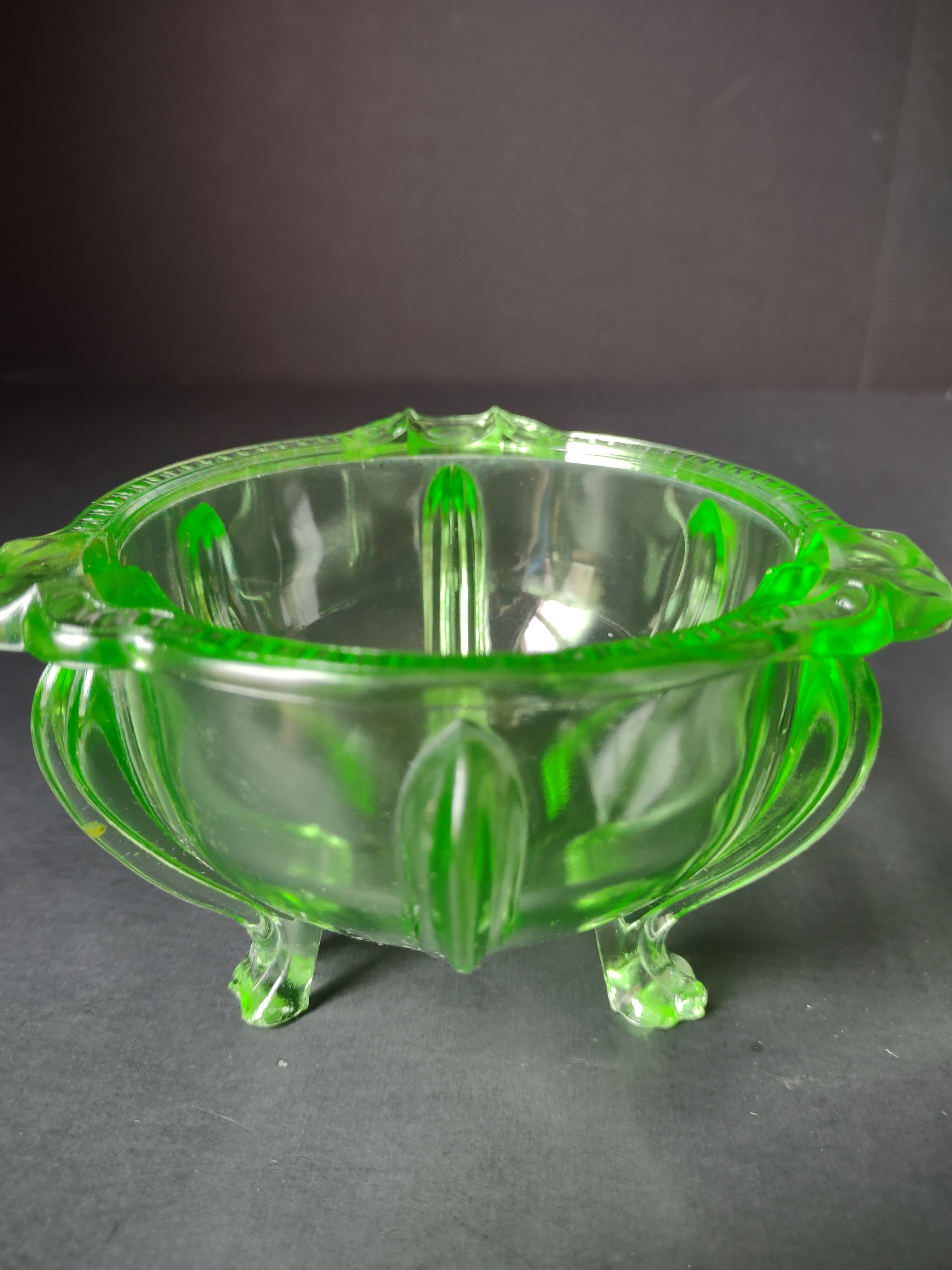 Vintage green uranium glass footed bowl angled view under UV black light