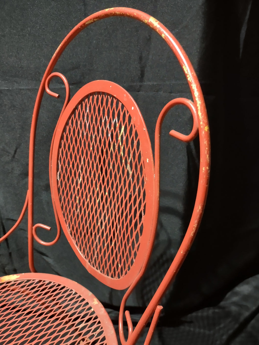 Vintage red metal mesh bistro chair - close-up of scrollwork back and mesh panel with paint wear