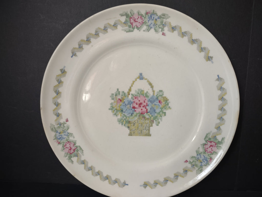 Vintage American Limoges Federal Sampler plate front view showing cross-stitch style flower basket center and zigzag ribbon border with pink and blue floral clusters