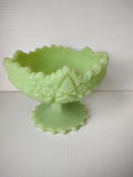 Vintage uranium vaseline glass footed compote with embossed star and grape pattern and sawtooth rim under natural light