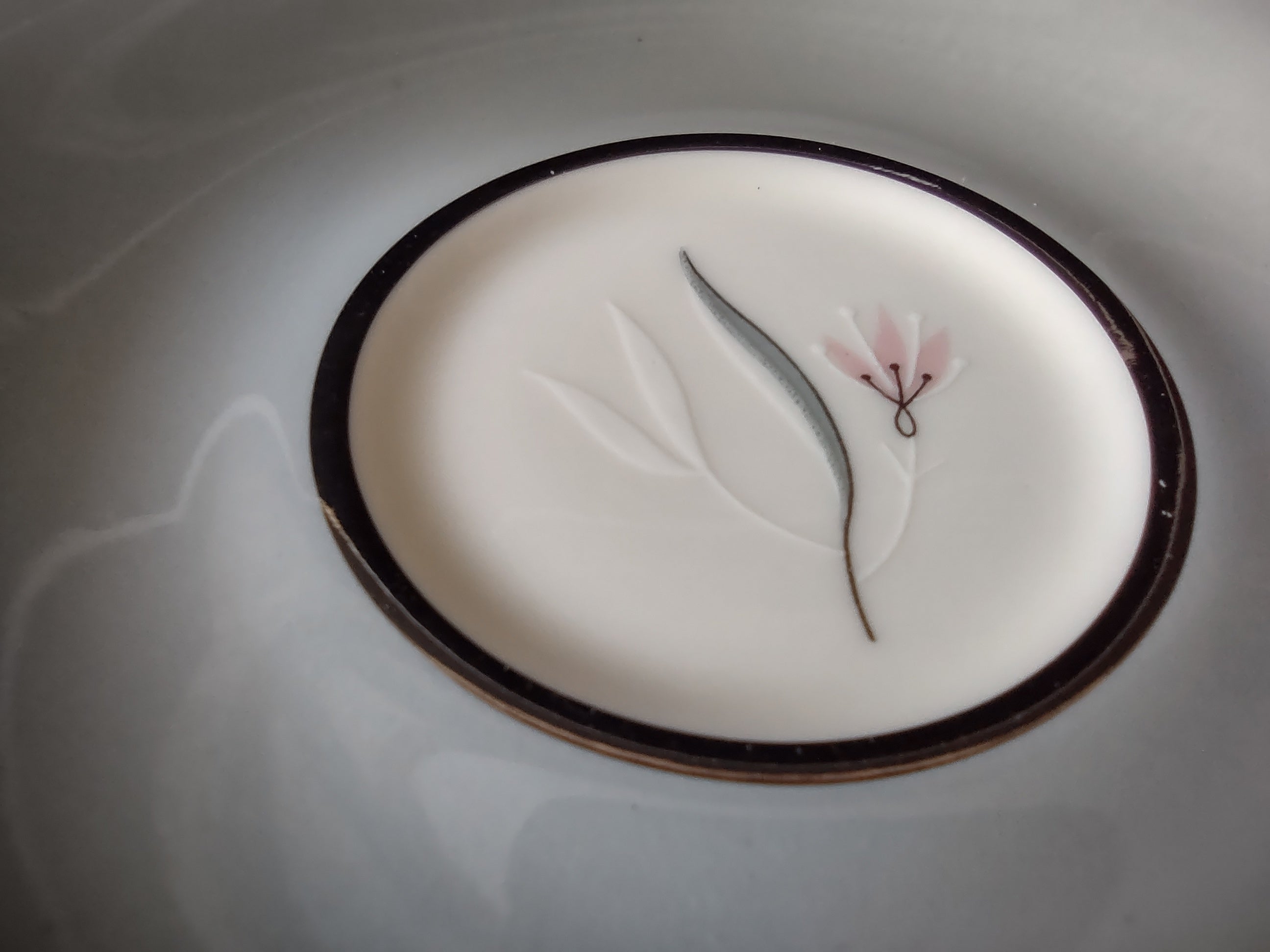 Castleton China Flair saucer close-up showing gray leaf and pink floral motif with dark platinum ring and gold rim
