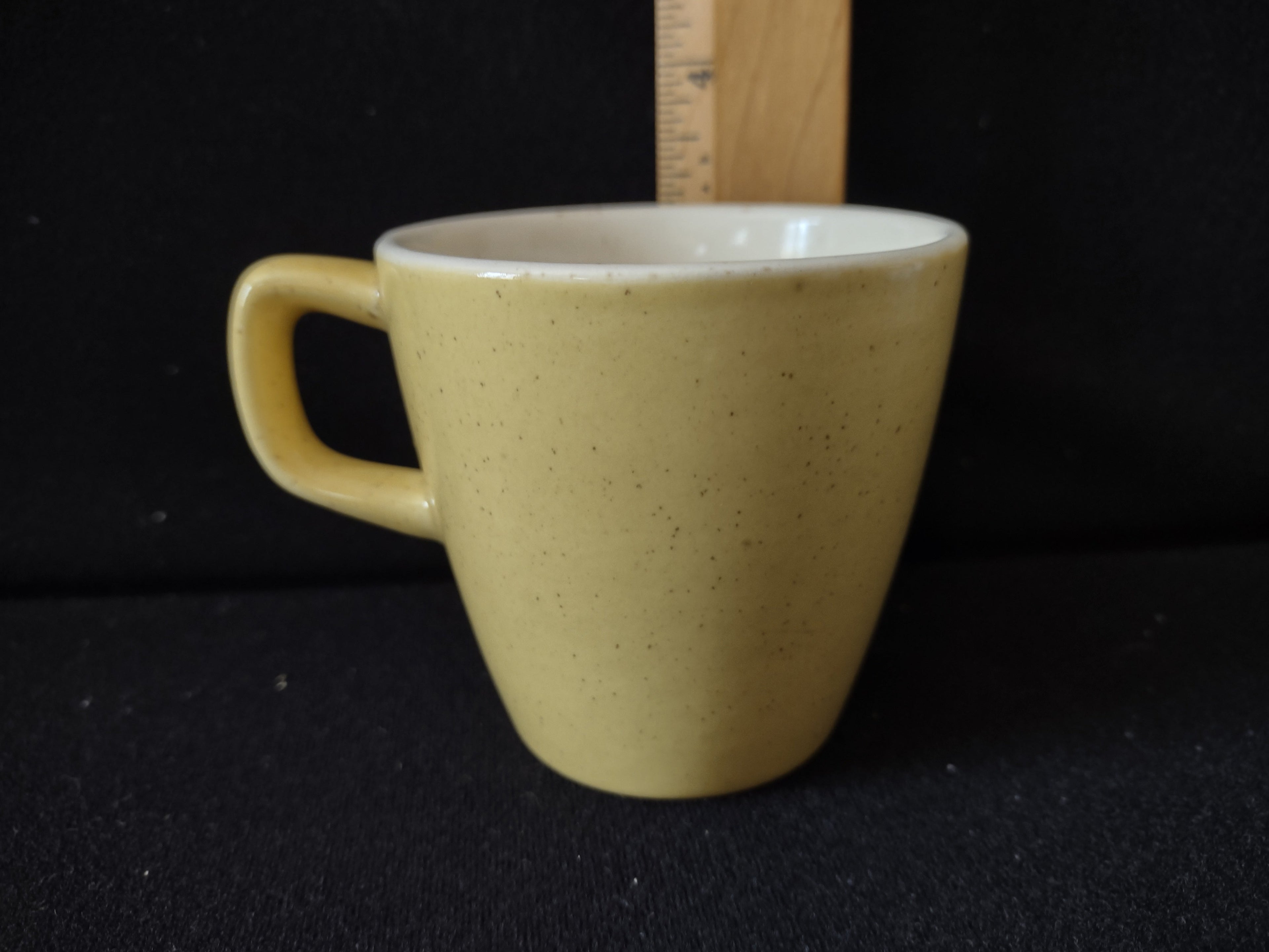 Vintage yellow speckled stoneware coffee cup with ruler showing height