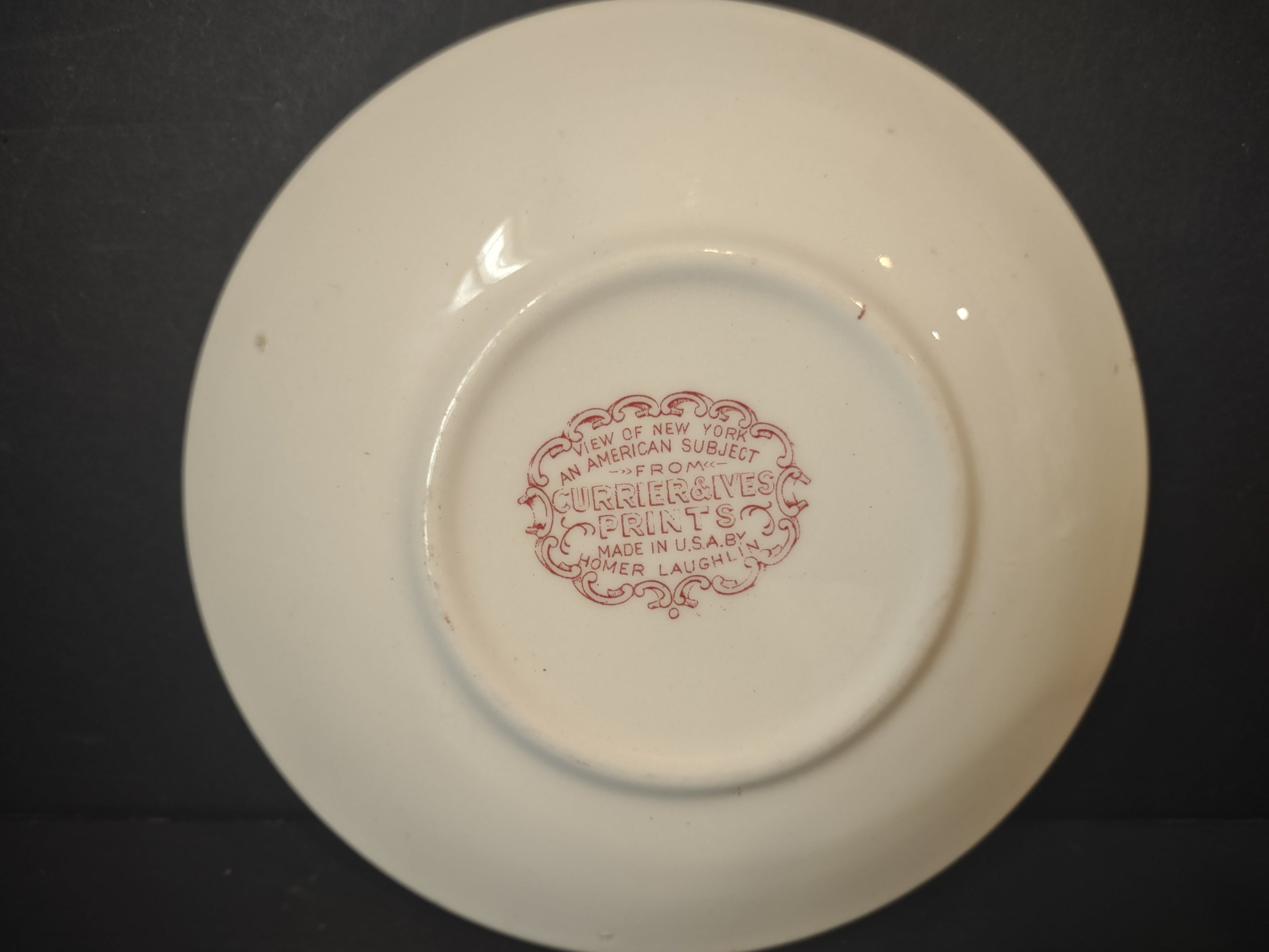 Front view of Vintage Homer Laughlin Currier & Ives red transferware saucer showing View of New York pastoral winter scene with cranberry leaf border