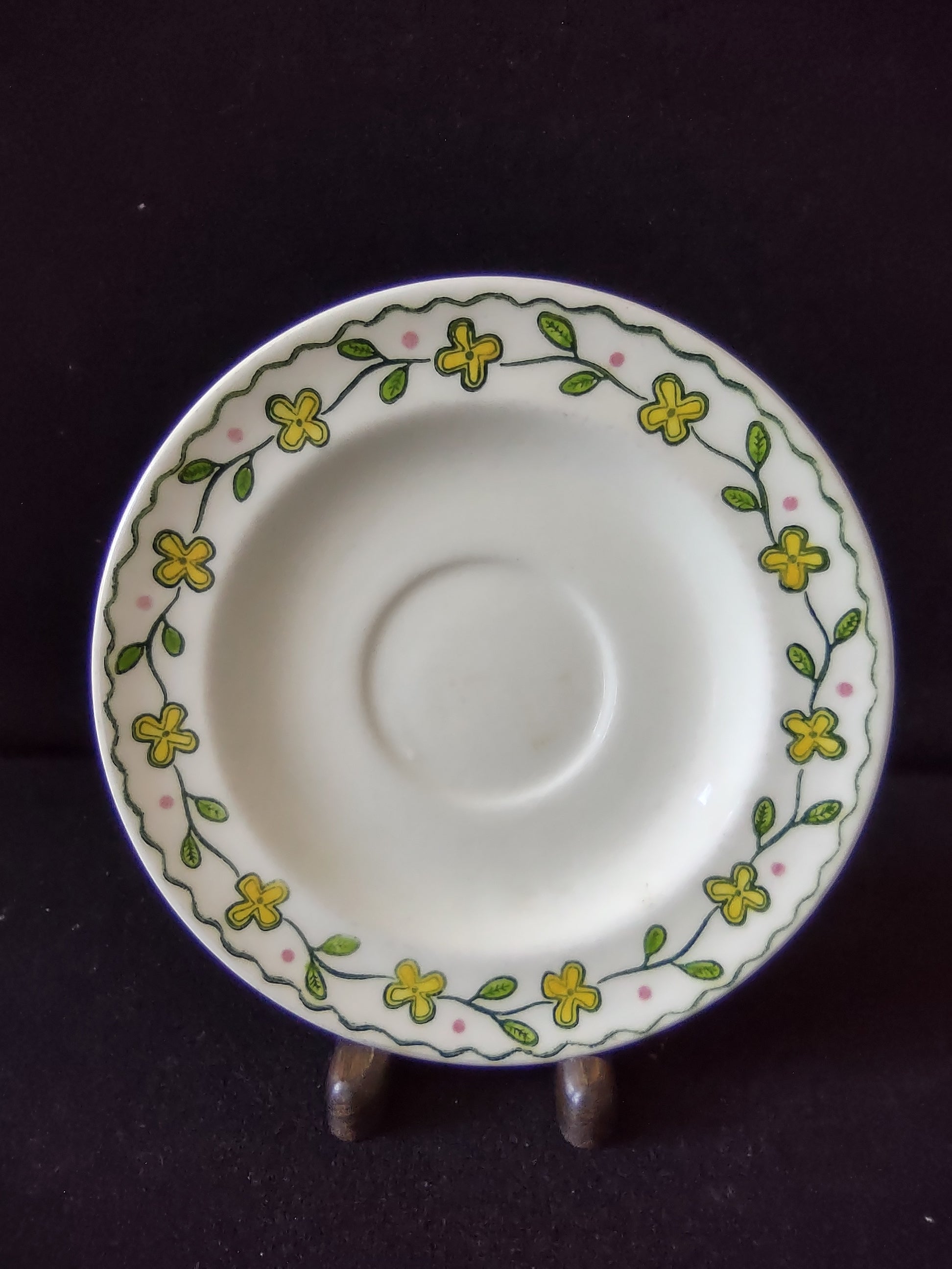 Close-up of Watt Pottery Happy Time pattern showing yellow four-petal flowers and green vine on saucer rim