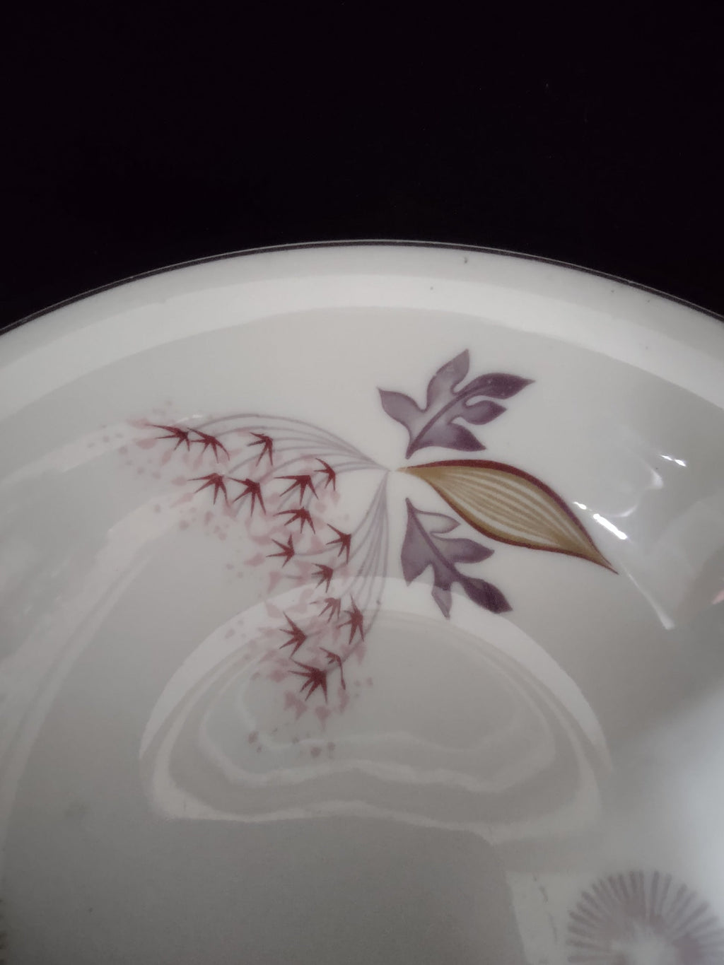 Close-up of Theodore Haviland Meadow Lace saucer showing burgundy starburst sunburst medallion motif and a faded worn medallion below, with discoloration consistent with age