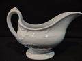 Vintage white porcelain footed gravy boat with embossed floral relief and loop handle, side view