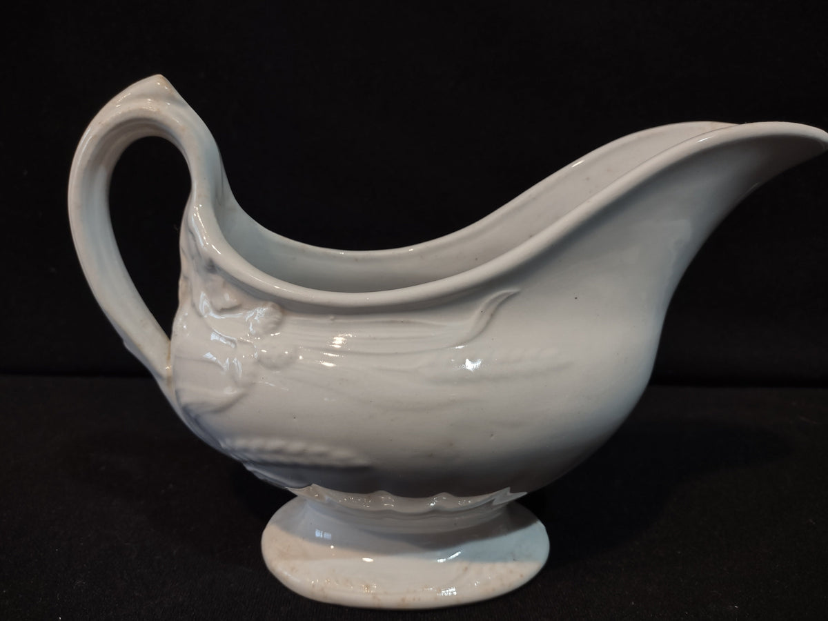 Vintage white porcelain footed gravy boat with embossed floral relief and loop handle, side view