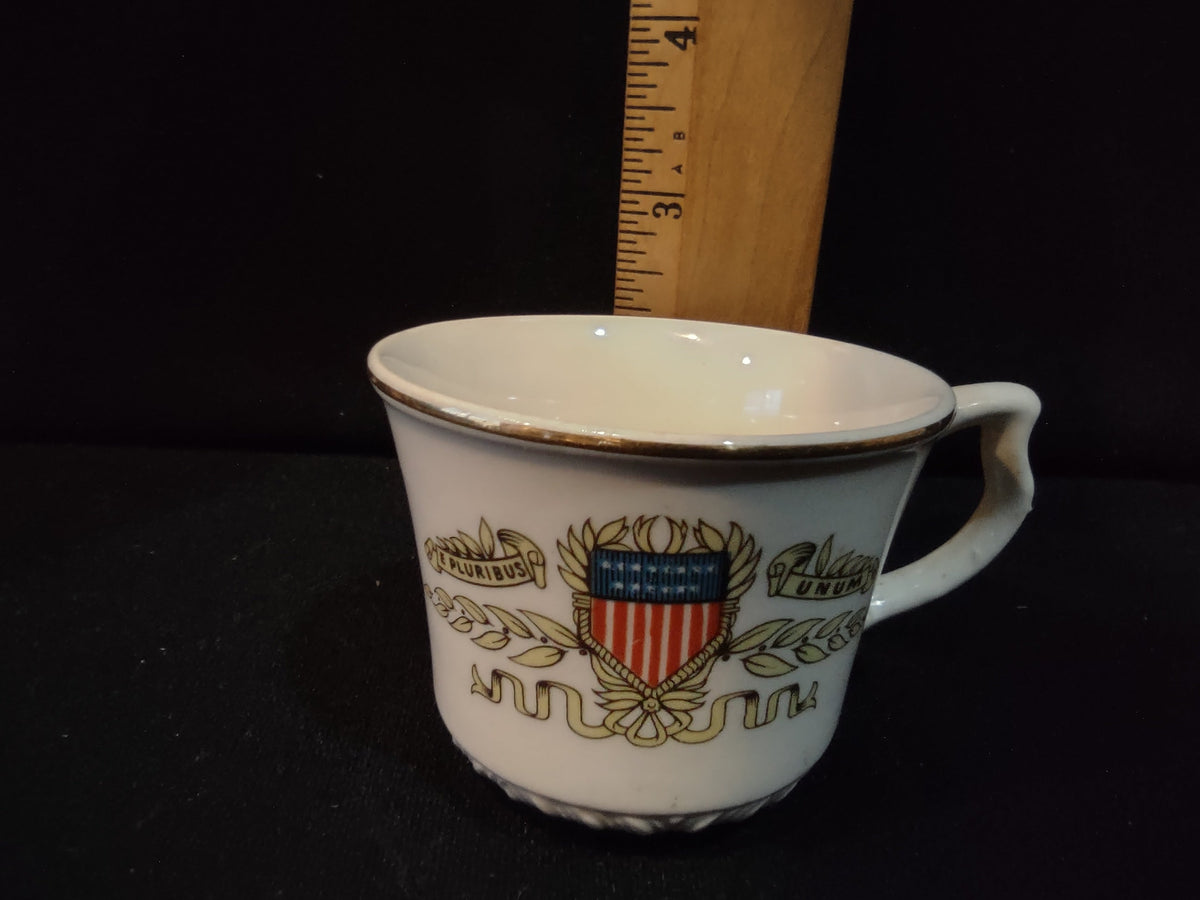 Vintage white porcelain tea cup with E Pluribus Unum American patriotic crest, red white and blue shield, gold laurel branches, embossed beaded base, gold rim, approximately 3 inches tall