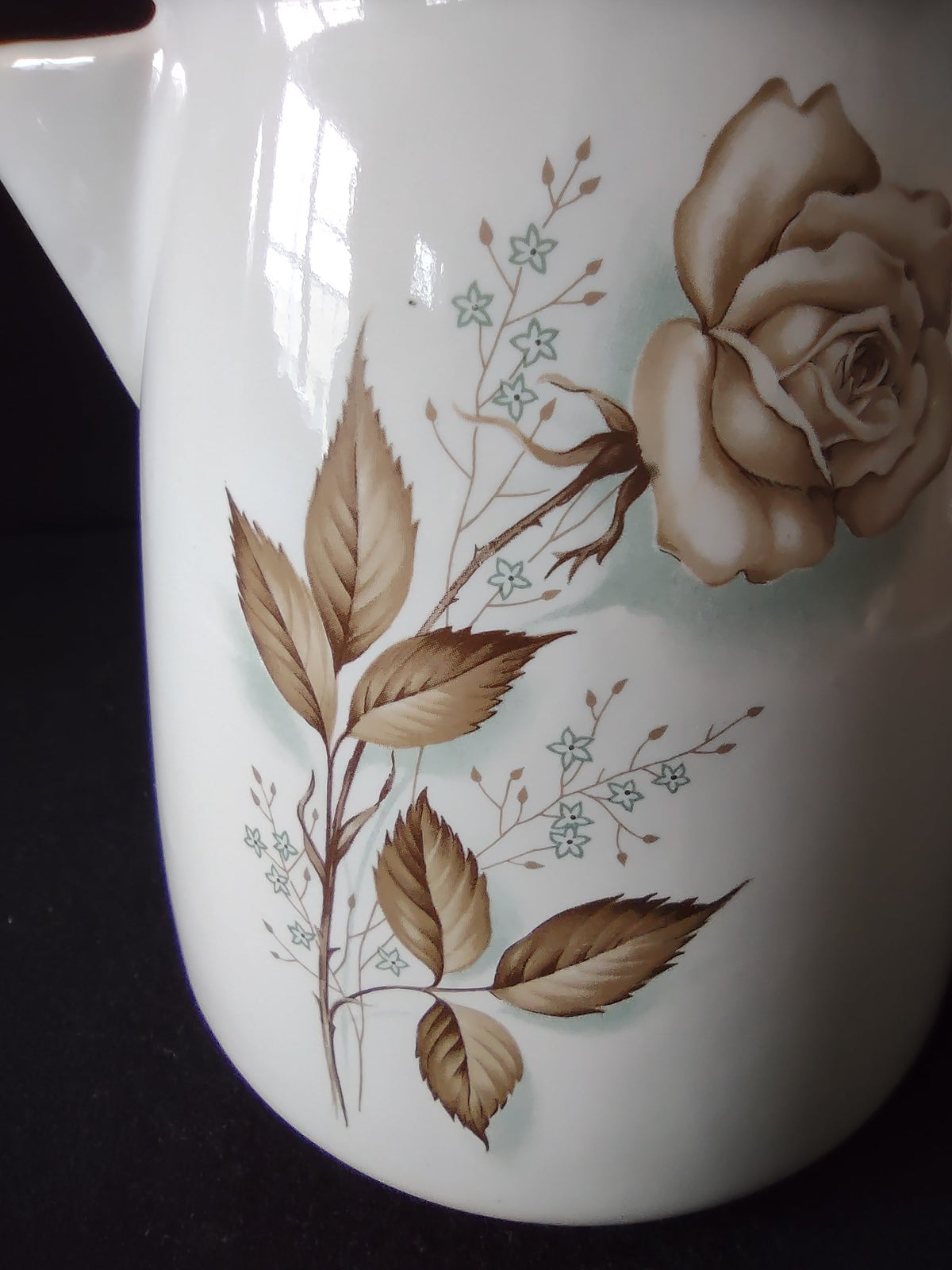 Close-up of brown sepia rose and blue forget-me-not floral pattern on vintage ceramic pitcher