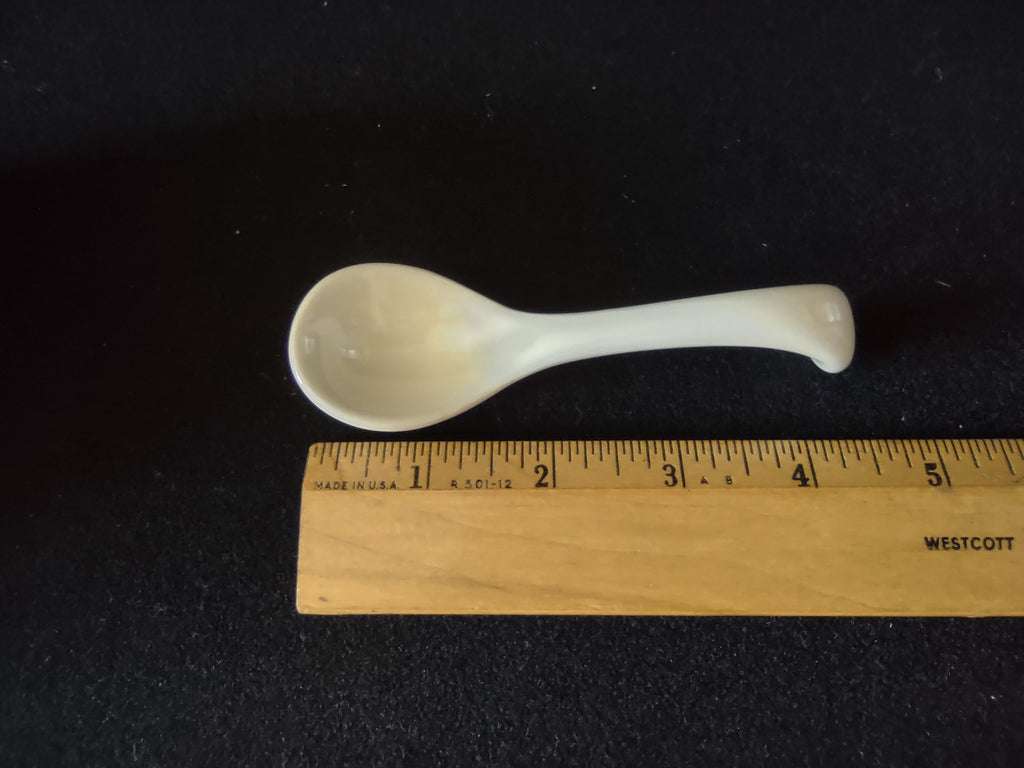 White ceramic spoon next to ruler showing approximately 4 inch length