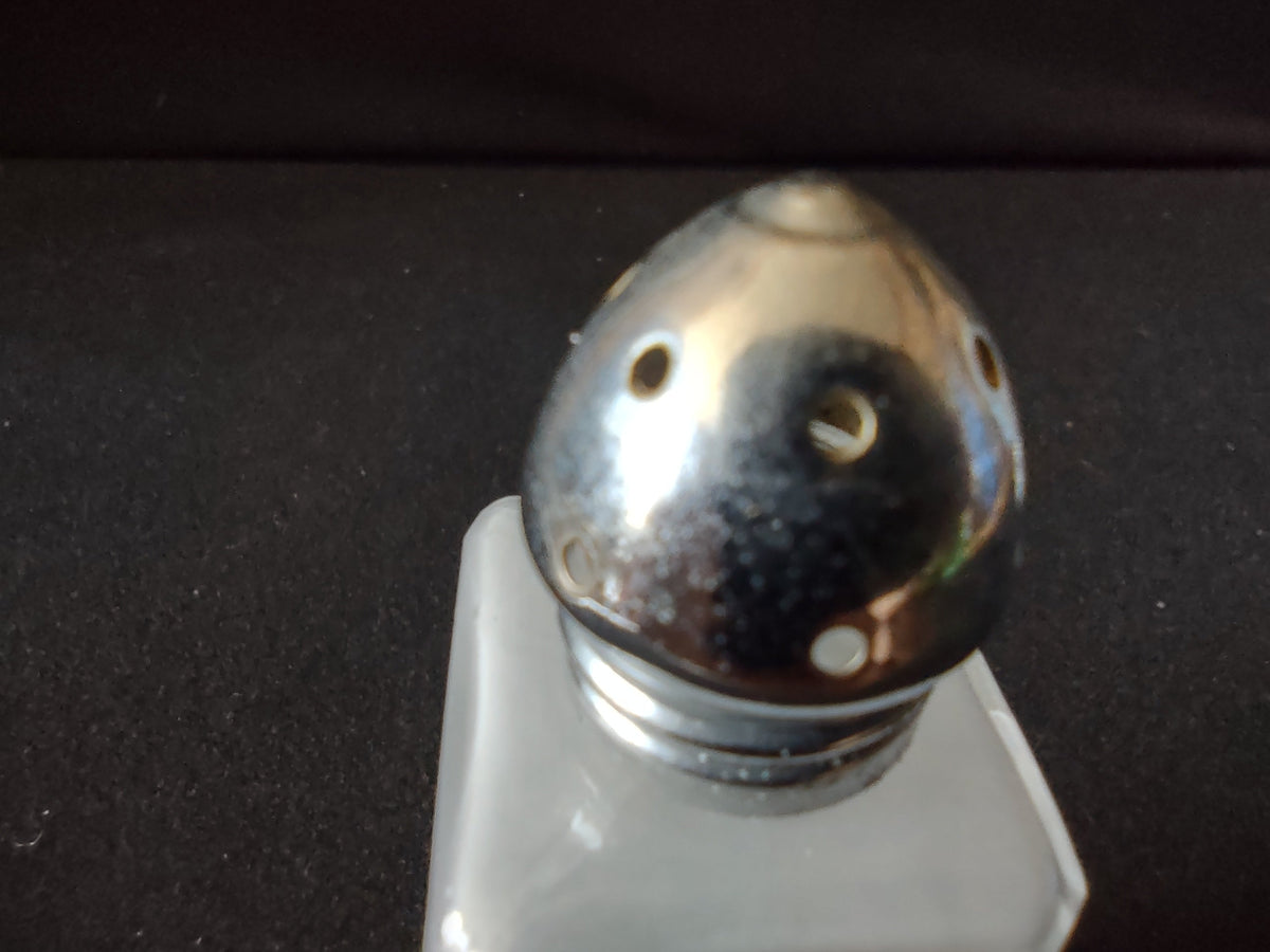 Bottom view of two vintage pressed glass salt and pepper shakers showing square bases with cut glass patterns
