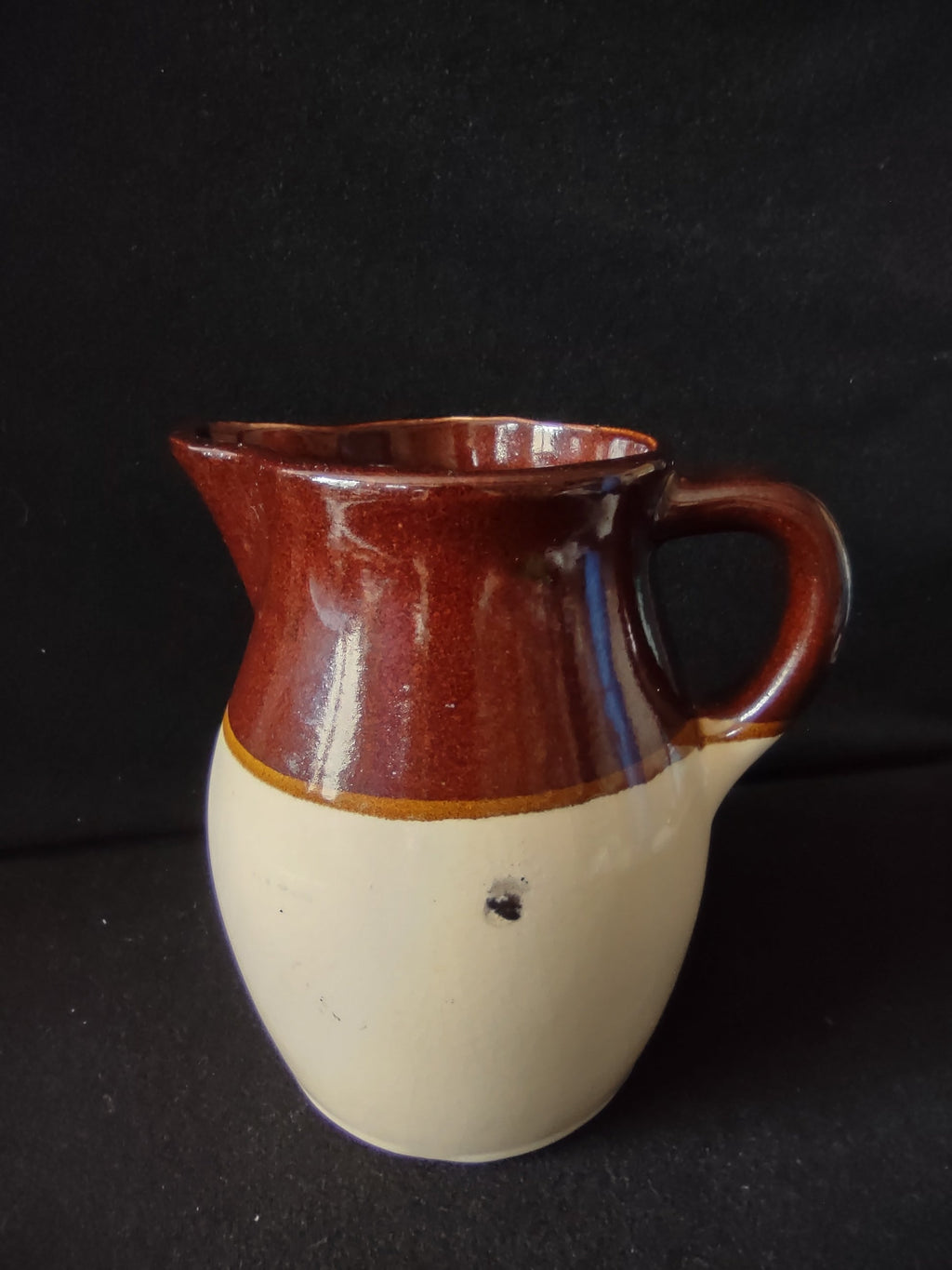 Close-up of dark spot glaze inclusion on lower cream body of vintage stoneware pitcher