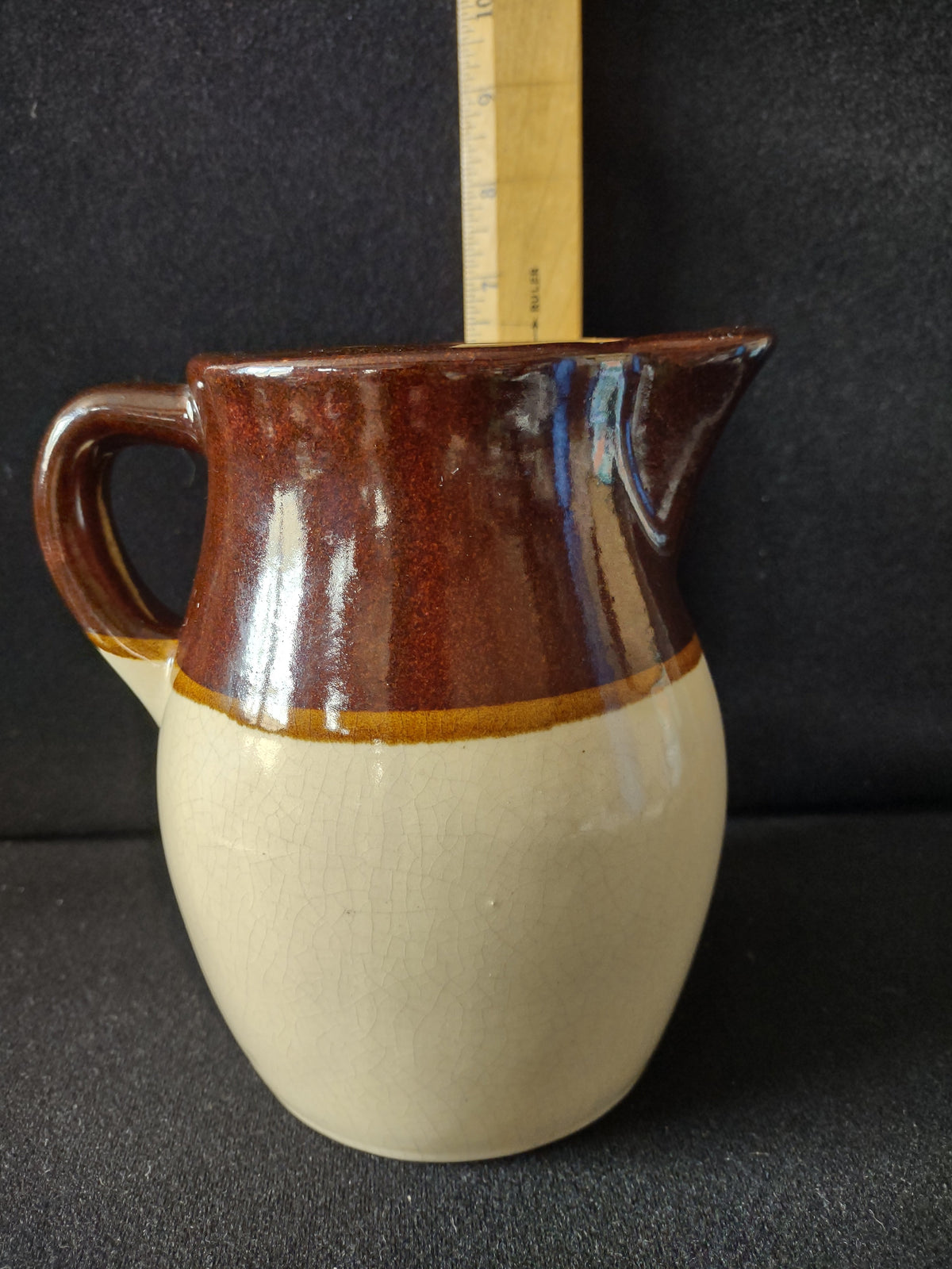 Front view of vintage two-tone stoneware pitcher showing brown upper half and cream lower half with loop handle