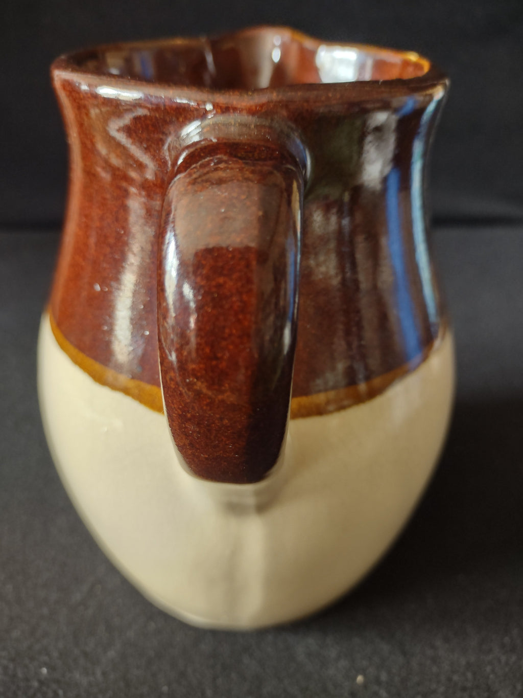 Back view of vintage two-tone stoneware pitcher showing cream lower body and brown upper glaze