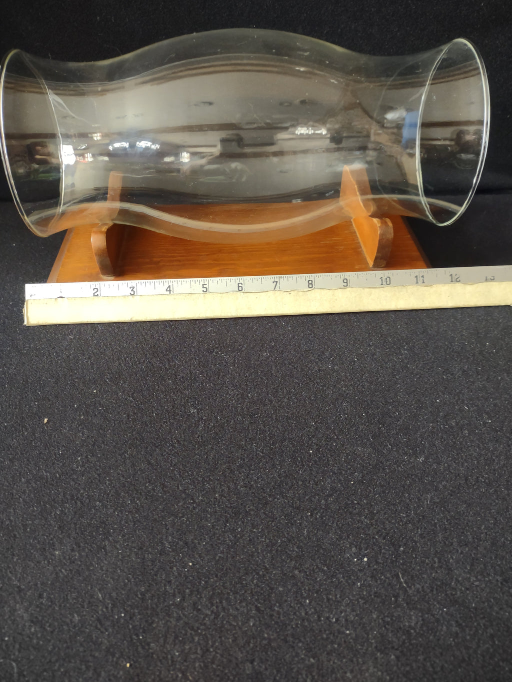 Side view of vintage clear glass hurricane shade resting on wood cradle stand