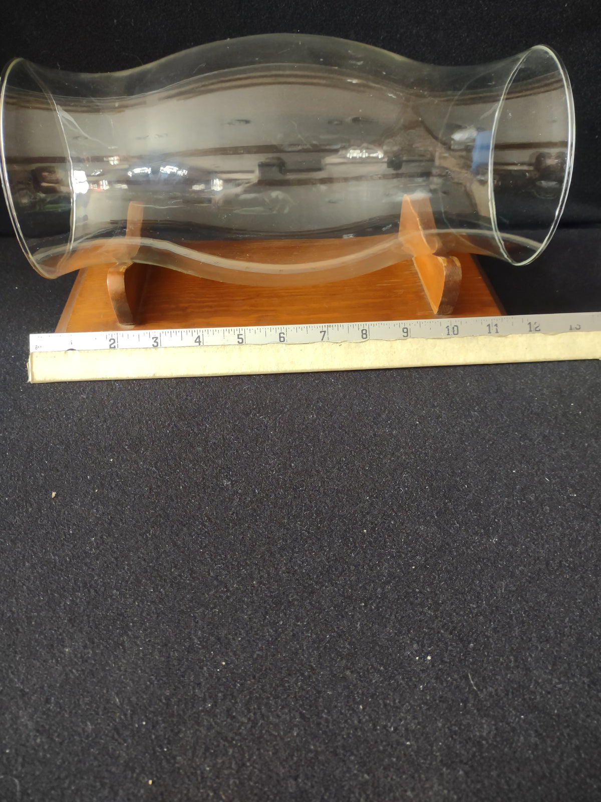 Side view of vintage clear glass hurricane shade resting on wood cradle stand