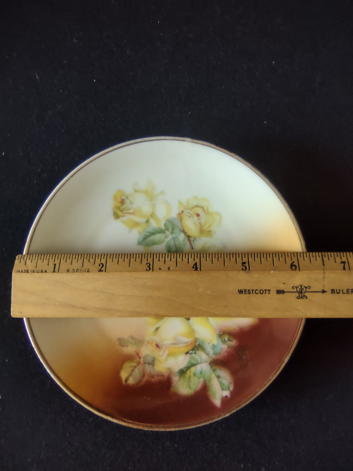 Hand-painted yellow roses plate close-up of lower center showing lush open yellow rose blooms and buds against deep mahogany burnt sienna graduated ground