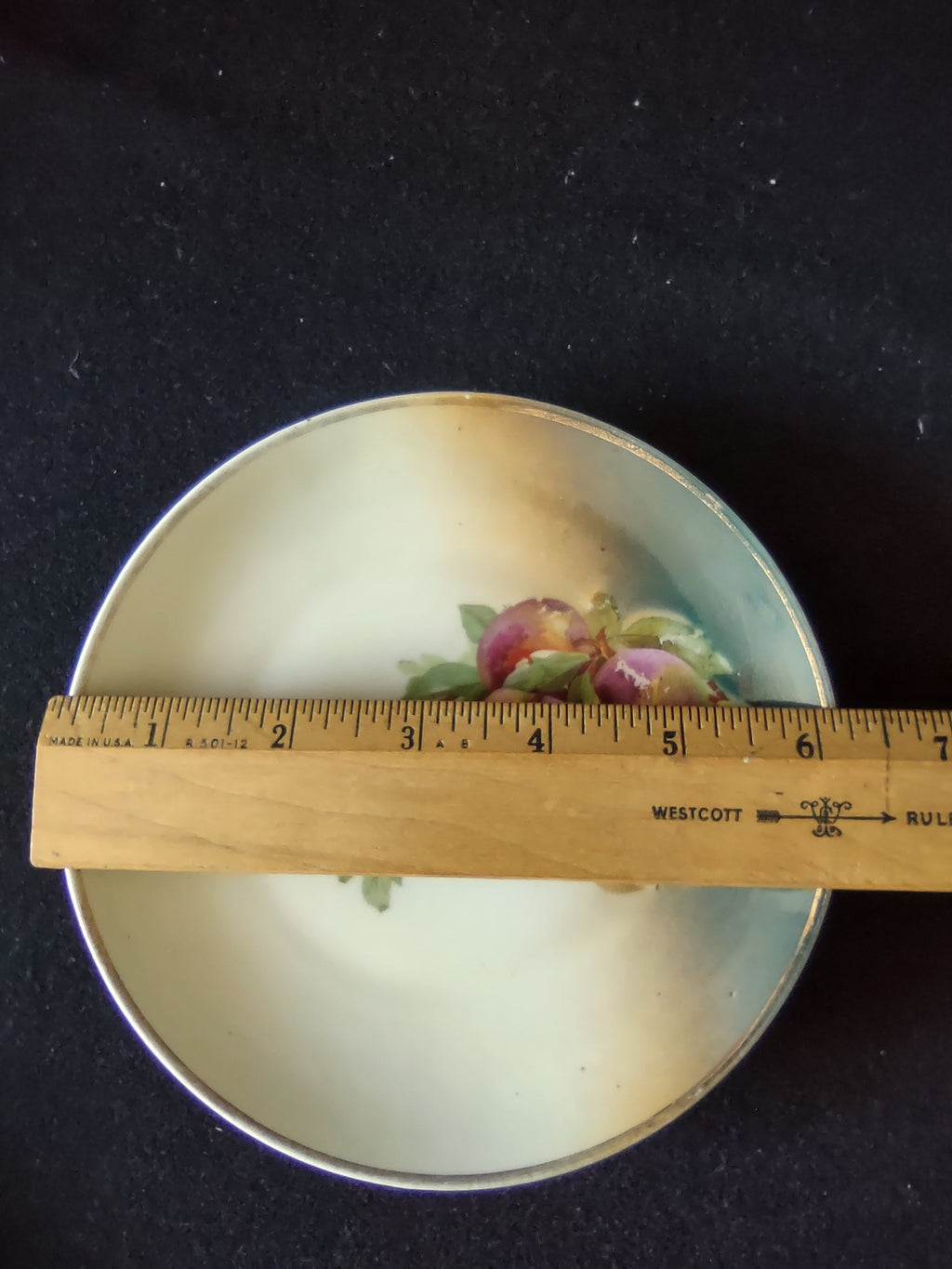 Hand-painted peaches Germany porcelain plate front view with ruler showing approximately 6 inch diameter on dark background with teal rim band