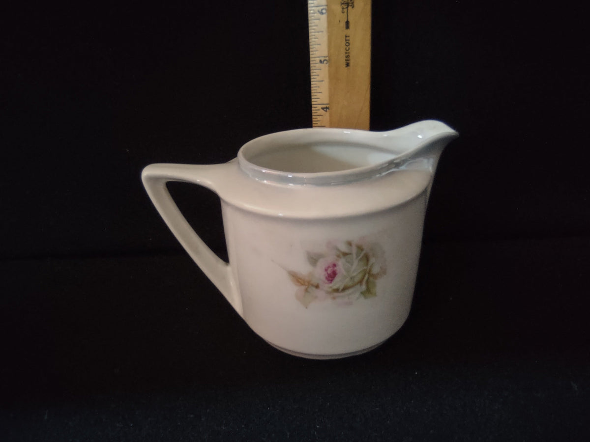 Vintage pink roses porcelain creamer close-up of front decoration showing large soft pink and cream cabbage roses with green foliage on off-white ground painterly style