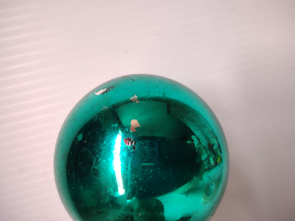Close-up of two silver metal caps and wire hangers on teal green glass ornaments