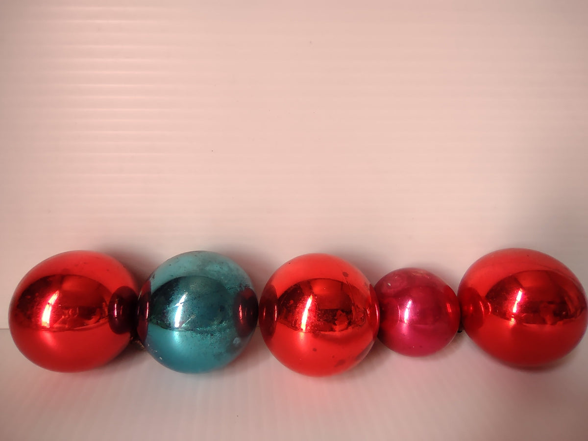 Close-up of three vintage glass ball ornaments — two red and one teal — showing metal caps and wire hangers
