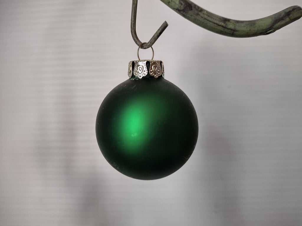 Vintage matte forest green glass ball Christmas ornament with ornate silver cap, hanging on branch