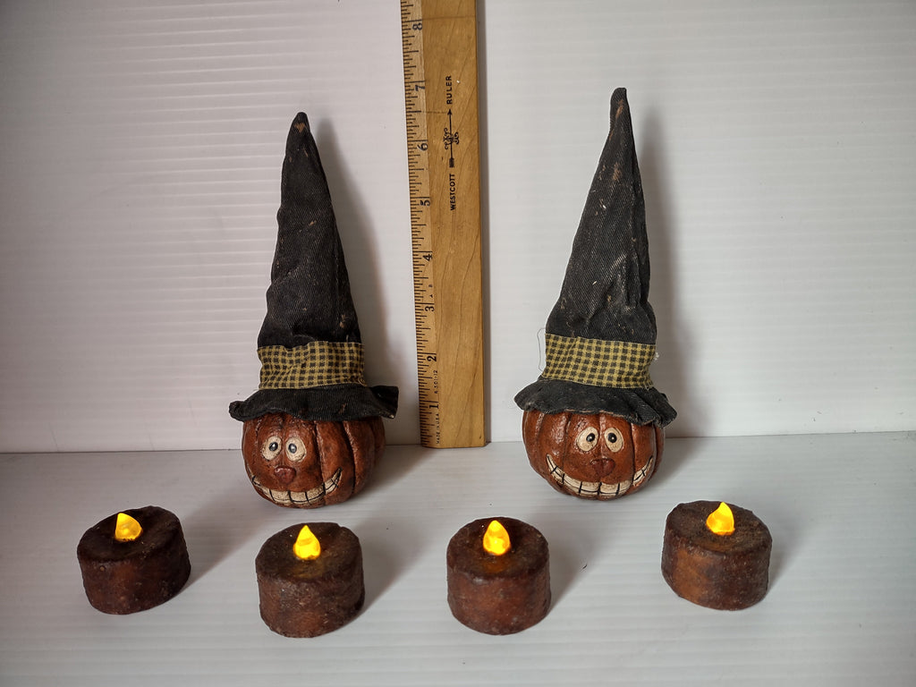 Primitive pumpkin witch hat figurines glowing with lit LED tealight candles in dark display