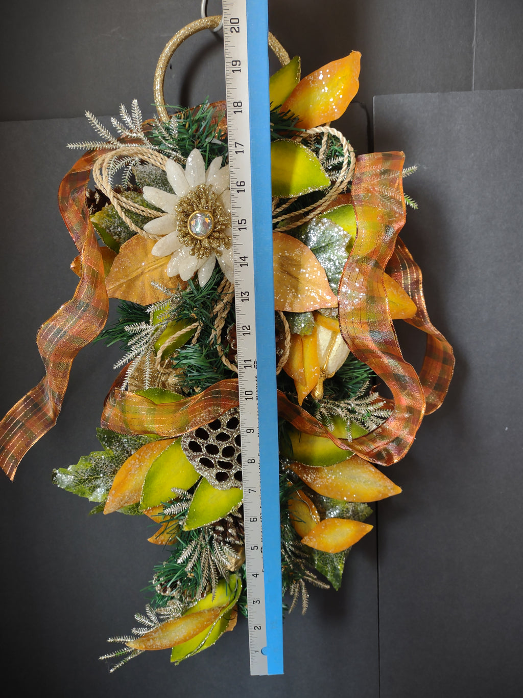 Decorative floral swag with orange ribbon gold and green foliage and off-white flower beside a ruler