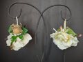 Two off-white and green floral fairy-style ornaments hanging from a black display stand