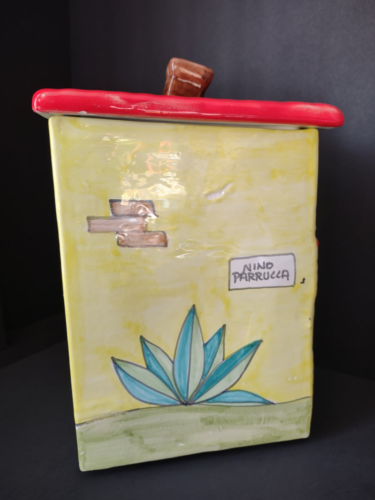 Side of ceramic bakery cookie jar with Nino Parrucca mark and painted blue green plant