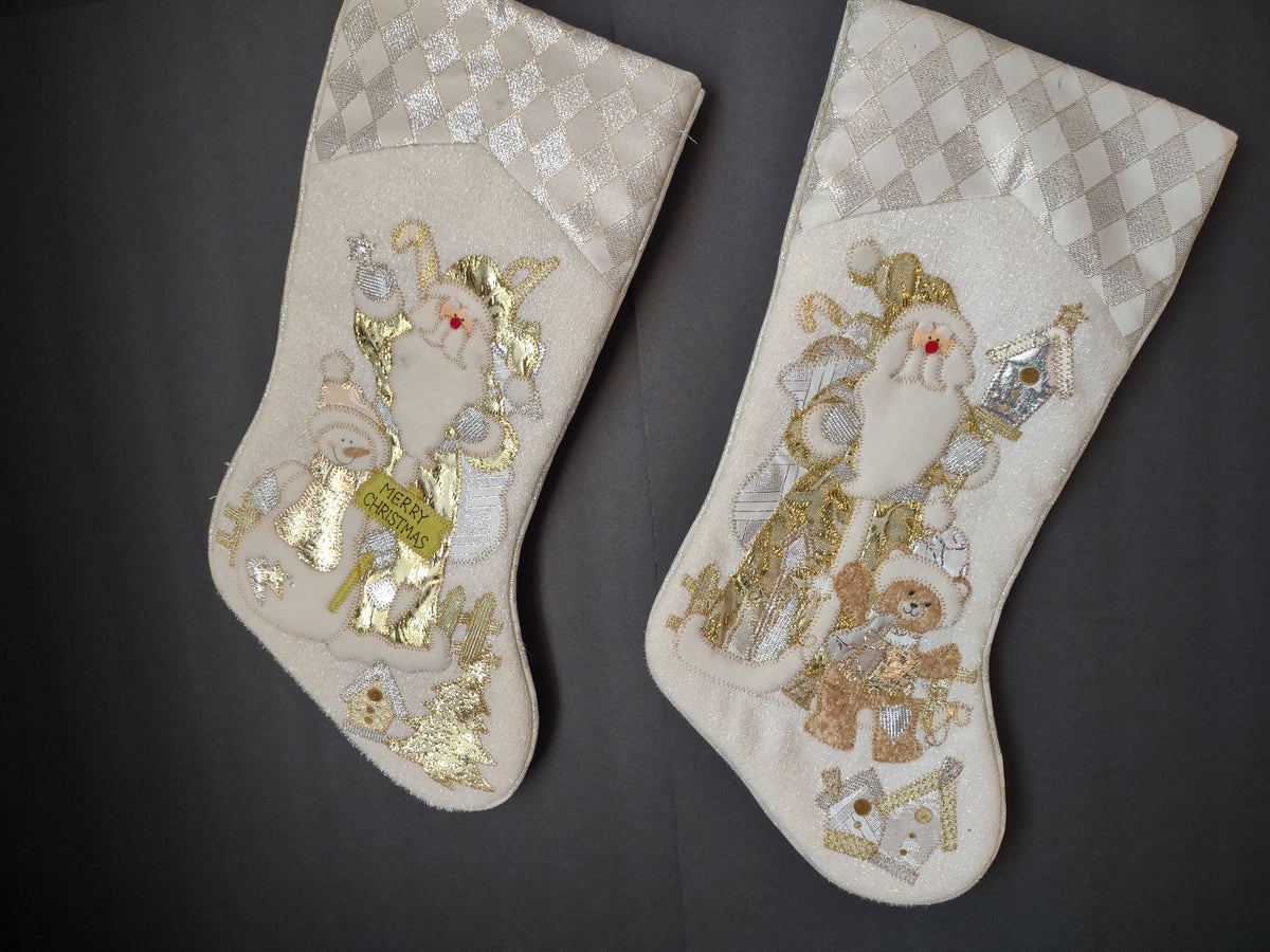 Pair of off-white Christmas stockings with gold and silver Santa teddy bear and house designs and diamond-pattern cuffs