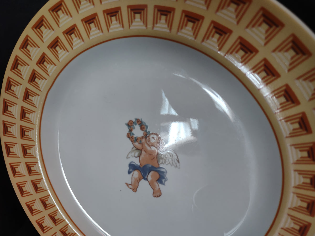 Close view of central cherub holding floral wreath on white plate center