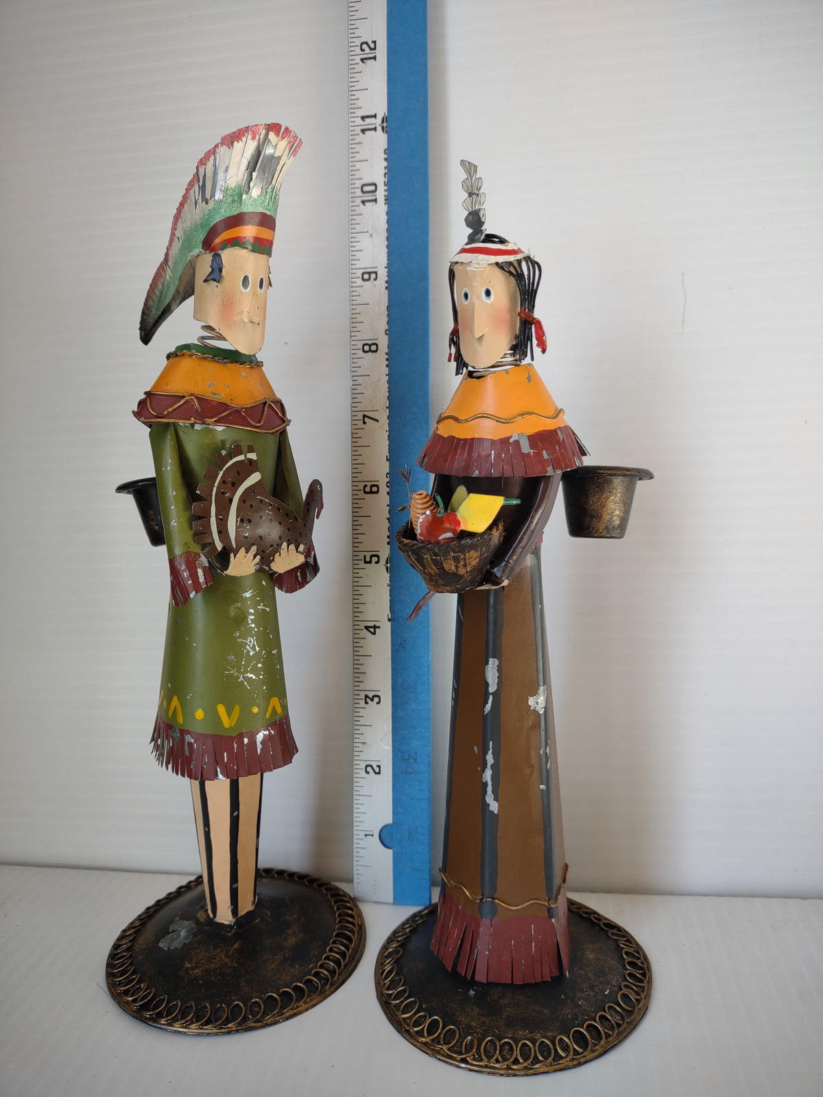 Pair of vintage painted metal Native American figures candle holders, one holding a turkey and one a basket of vegetables, shown beside a ruler