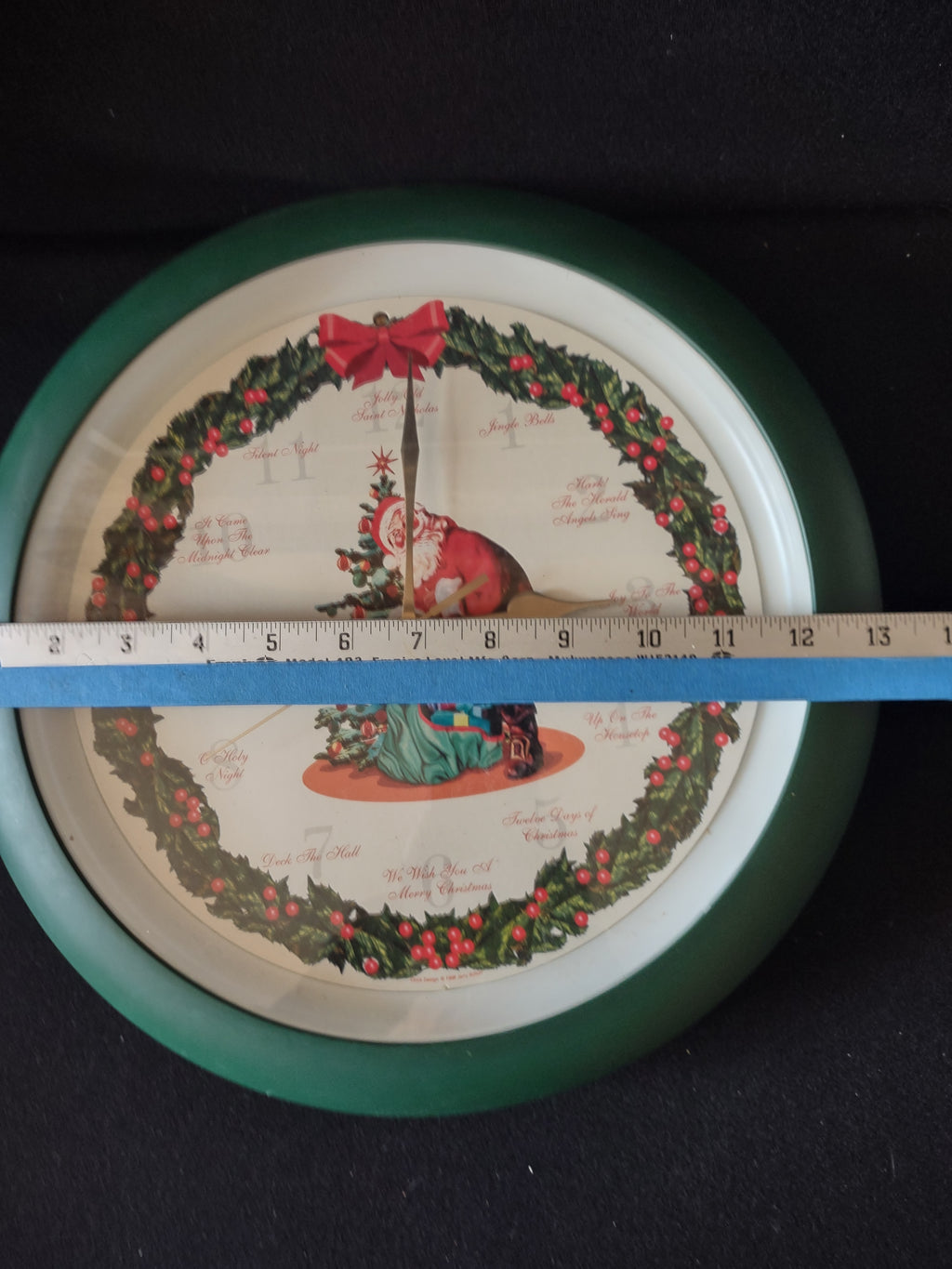 Santa Christmas wall clock with green rim and holly wreath shown with measuring tape