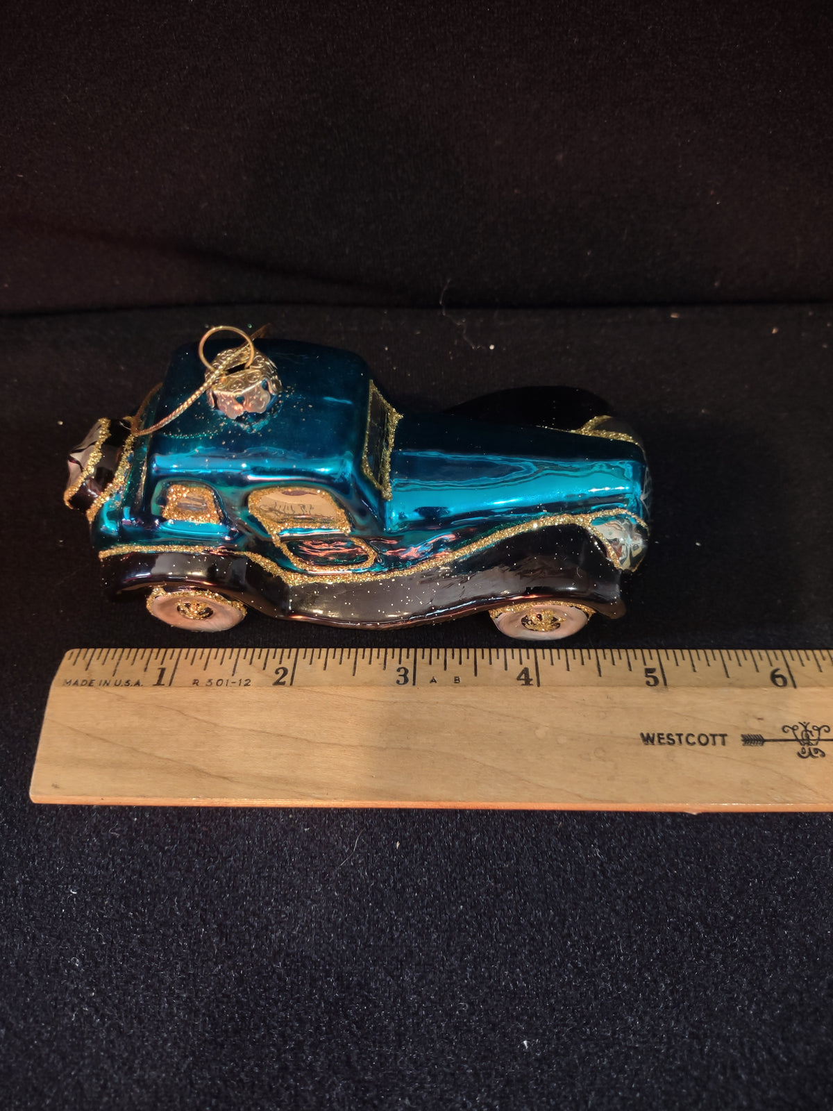 Turquoise glass car ornament beside ruler for size